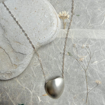Silver necklace with a pendant on a textured surface with dried flowers.